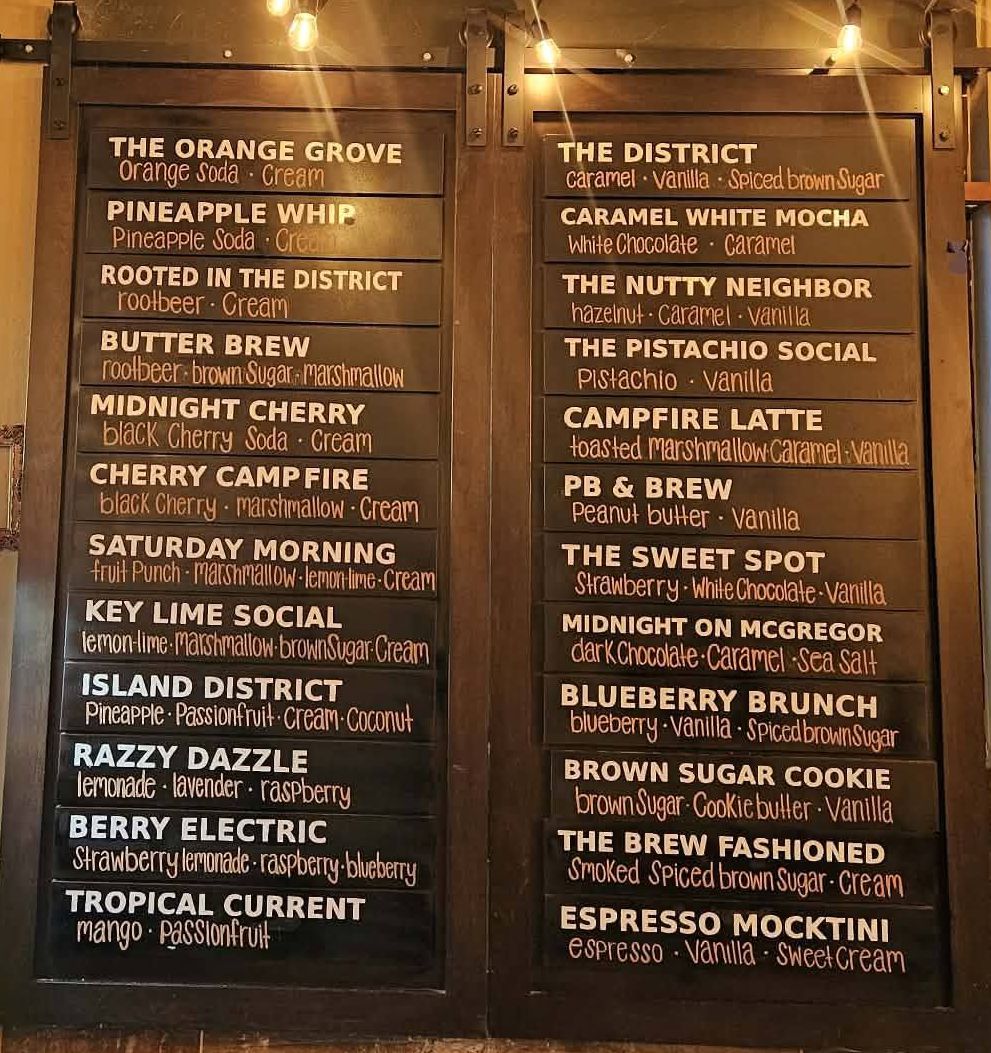 The Brew District café wall boards listing the 24 soda, refresher and signature coffee flavors transcribed above.